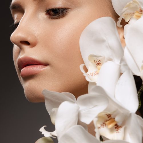 Portrait of beautiful young woman with nude make up posing with orchid flowers isolated over dark background سلامتی و زیبایی پوست و مو | پریرو